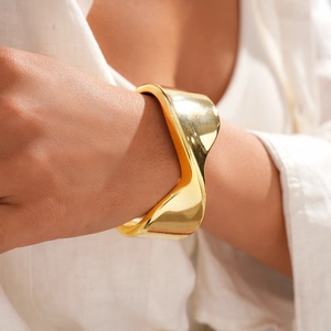 Close-up of chunky gold wave bangle on wrist showcasing polished metallic texture