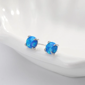 Macro view of blue opal earrings with silver four-prong setting on white background