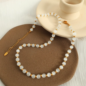 Elegant gold titanium steel necklace with white cat eye beads on ceramic tray