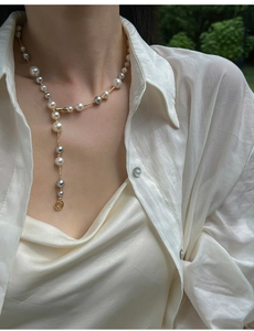 Detail of Y-shaped pearl necklace with white and grey beads worn on a white shirt