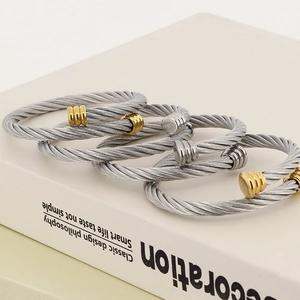 Three-piece stainless steel cable wire wrap bracelets in silver and gold on a white book