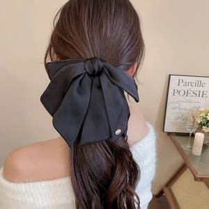 Detail of a large black satin bow hair claw clip worn on long hair in a cozy setting