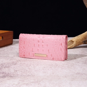 Pink crocodile pattern wallet with gold metal hardware on elegant stone background