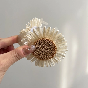 Macro detail of a raffia woven white daisy hair claw clip with a brown center piece