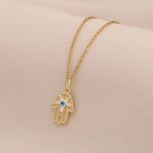 Detailed close-up of golden Hamsa Hand pendant with crystal inlay on beige fabric
