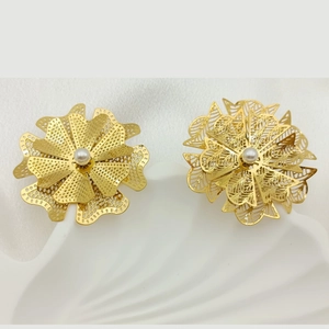 Macro shot of gold floral hollow earrings with white pearl center on shell props