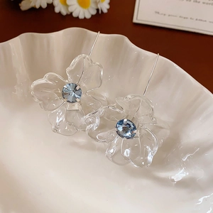 Detail view of transparent resin flower earrings with blue crystal centers on shell tray