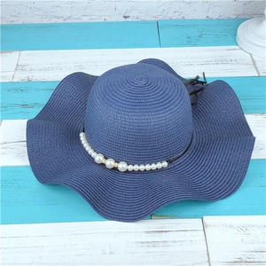 Detail of navy blue straw sun hat featuring wavy wide brim and pearl decoration