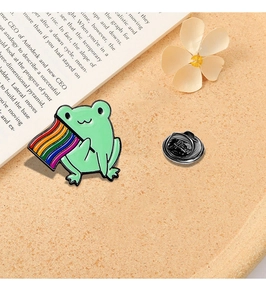 Close-up of cute green cartoon frog enamel pin with a rainbow flag and butterfly clutch