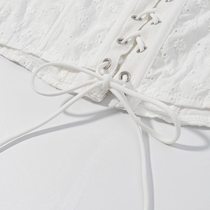 Dettaglio del corsetto bianco con ricami floreali e chiusura con lacci e nastri sottili