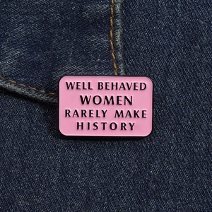 Detail of pink enamel brooch with black text pinned on blue denim fabric background