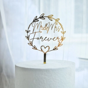 Detailed view of a golden acrylic Mr & Mrs Forever cake topper with a heart wreath design