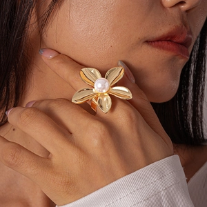 Detailed view of large gold metallic five-petal flower ring with central pearl on finger