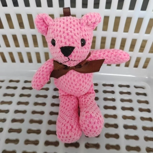 Detailed macro view of pink knit teddy bear plush featuring a brown ribbon bow detail