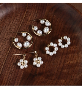 Detailed view of three styles of flower and circle gold pearl earrings on a wooden tray