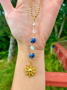 Detailed shot of golden sun pendant with colorful crystal beads held in hand outdoors