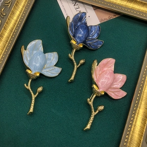 Detailed close-up of three enamel magnolia brooches in blue and pink on green velvet