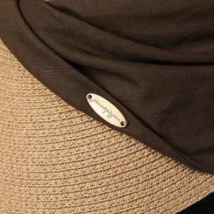 Close-up of straw woven sun hat featuring a dark brown knit band and golden metal logo tag
