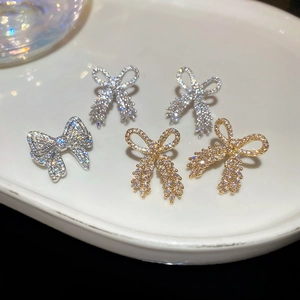 Close-up of three pairs of sparkling bow earrings in gold and silver with full zircon stones