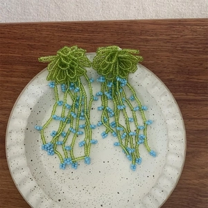 Close-up of handmade green and blue beaded flower tassel earrings on a ceramic dish