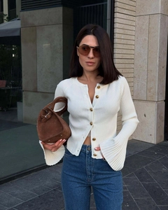 Detail of white ribbed knit cardigan with gold buttons and elegant bell sleeves