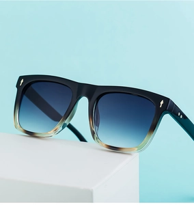 Detail of square gradient sunglasses with blue lenses and gold rivet accents on blue background