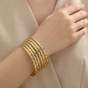 Detail of layered gold bangles with diamond-cut rhombus textures worn on a model's arm