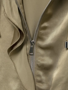 Macro detail of silver metal zipper and khaki satin fabric texture on street jacket