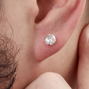 Close-up of a gold zircon stud earring with a four-prong setting worn on the earlobe