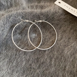 Detail view of large silver hoop earrings on grey faux fur with a thank you card