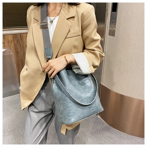 Detail of blue faux crocodile texture bucket bag with wide adjustable fabric strap