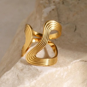 Detailed view of layered wavy gold ring placed on natural textured stone background