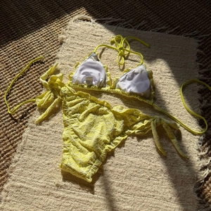 Close-up of bright yellow bikini with white floral embroidery textures on woven mat