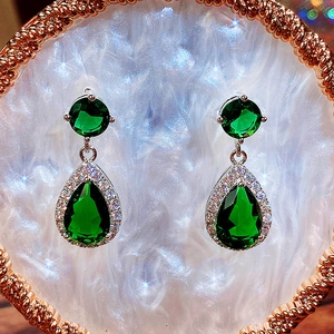 Macro shot of emerald green teardrop earrings with a sparkling halo setting and silver base