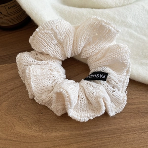 Detail of a beige knitted scrunchie with a Fashion label on a rustic wooden background
