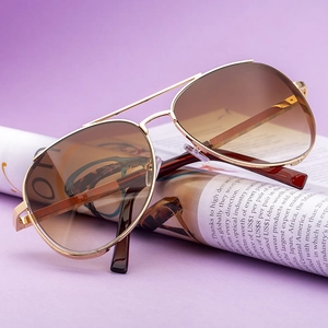Classic aviator sunglasses with gold metal frame and gradient brown lenses on purple background