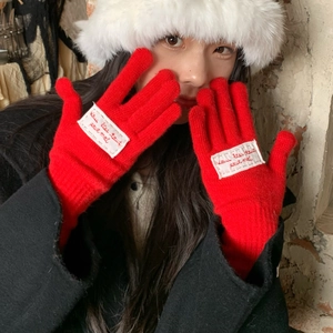 Detail of red knit glove with a white fabric patch showing French embroidery text