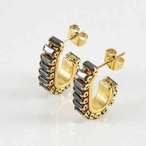 Detail of gold U-shaped earrings with rectangular black zircons on reflective background