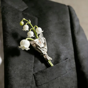 Detailaufnahme einer Maiglöckchen-Brosche an einer schwarzen strukturierten Anzugtasche