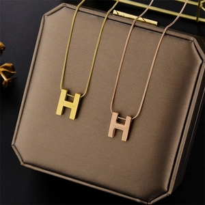 Macro detail of H-shaped letter necklaces in gold and rose gold finish on jewelry box