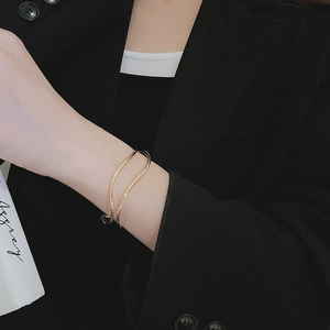 Detail of gold wavy open bangle worn with a black blazer for a minimalist fashion look