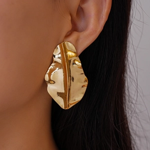 Close-up of a model wearing a golden metallic leaf-shaped earring with wrinkled texture