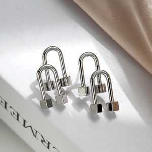 Irregular silver U-shaped geometric stud earrings with cube ends on a book background