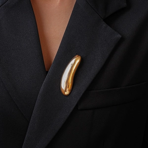 Detail of a liquid-effect gold metal brooch on a textured black blazer lapel