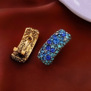 Détail de boucles d'oreilles dorées vintage avec cristaux bleus sur satin rouge foncé