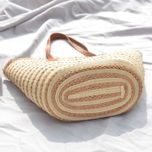 Handmade woven straw tote bag with brown leather handles and striped texture
