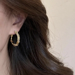 Detail of gold hoop earrings featuring textured woven patterns on a model wearing them