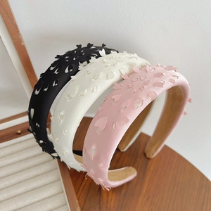 Three silk hollow heart headbands in black, beige, and pink colors on wood box