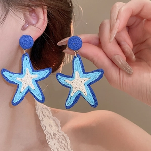 Detailed close-up of blue raffia woven starfish earrings worn on a female ear
