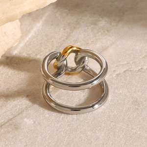 Doppio anello in acciaio inossidabile lucido con maglia dorata su sfondo pietra